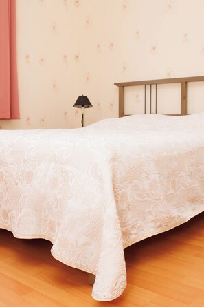 A bedroom with a wooden bed frame, a white bedspread with a floral pattern, a bedside lamp, and a wall with a floral wallpaper. - Maison familiale, Proche Saint-Emilion (Pujols)