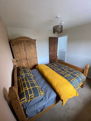 A bedroom with a wooden bed, two pillows, a bedside table, and a wardrobe. - Blissful Retreat - 4 Bedroomed House (Bridgend)