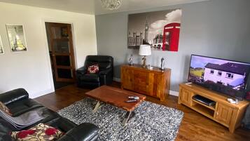 A living room with a sofa, coffee table, TV stand, and a painting of London landmarks.