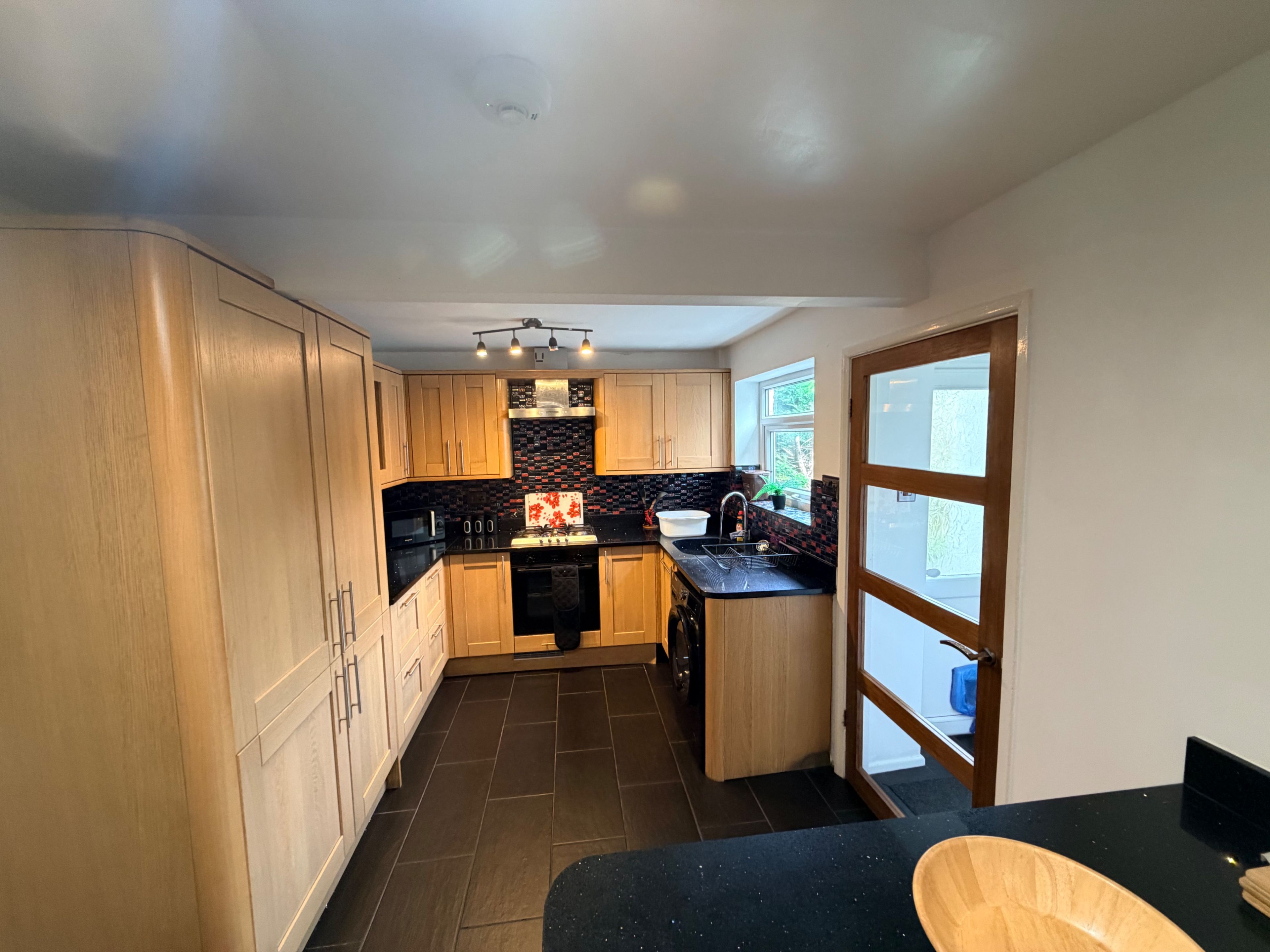 A compact kitchen with wooden cabinets, a black countertop, and a window providing natural light.