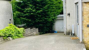 A narrow driveway leading to a garage, surrounded by a concrete wall and a large tree.