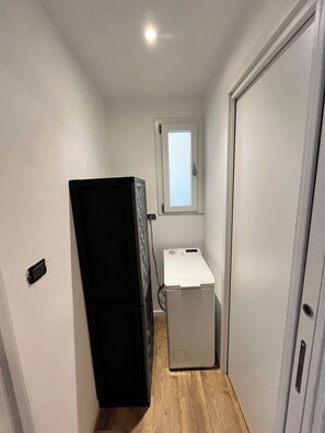 Ein kleines Zimmer, ausgestattet mit einer Waschmaschine, einem Kühlschrank und einer Tür mit Fenster.