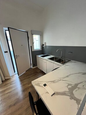 Eine kompakte Küche mit integriertem Geschirrspüler, Spüle und einem Fenster über der Arbeitsfläche.