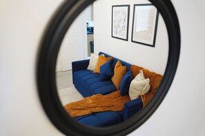 Un divano blu con numerosi cuscini, una coperta marrone e due quadri appesi al muro.