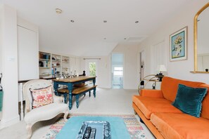 Ein geräumiges Wohnzimmer mit einem großen, orangefarbenen Sofa, einem Holzespeisetisch und einem weißen Sessel mit einem floralen Kissen.