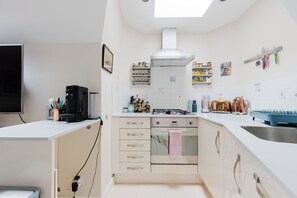 Cocina compacta con estufa a gas, horno y cafetera sobre la encimera.