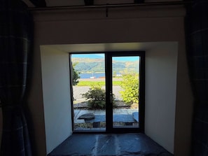 Quarto com uma grande janela que oferece vista para um lago, colinas e um píer com um barco.