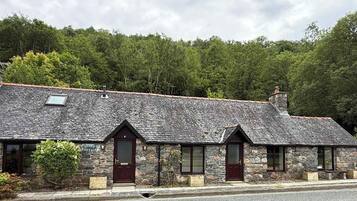 A stone cottage with a sloped roof, a wooden door, and a small window.