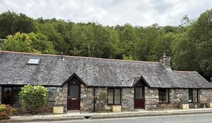 A stone cottage with a sloped roof, a wooden door, and a small window.