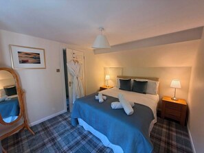 Ett hotellrum med en säng, två sängbord med lampor, en spegel, en inramad tavla på väggen och en dörr där en badrock hänger.