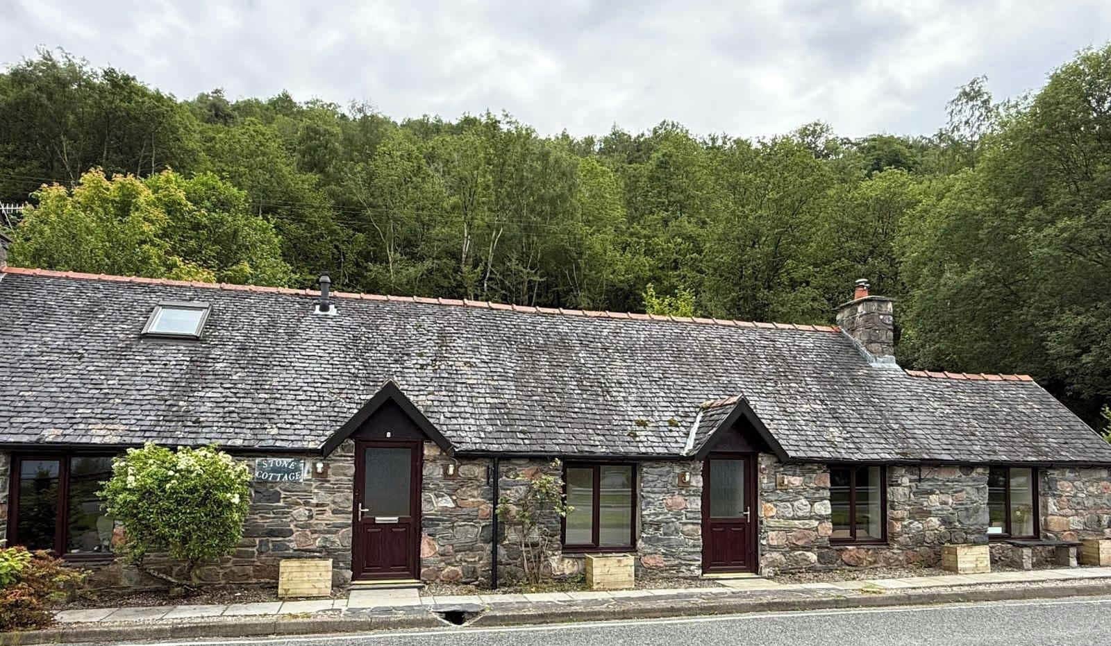 A stone cottage with a sloped roof, a wooden door, and a small window.