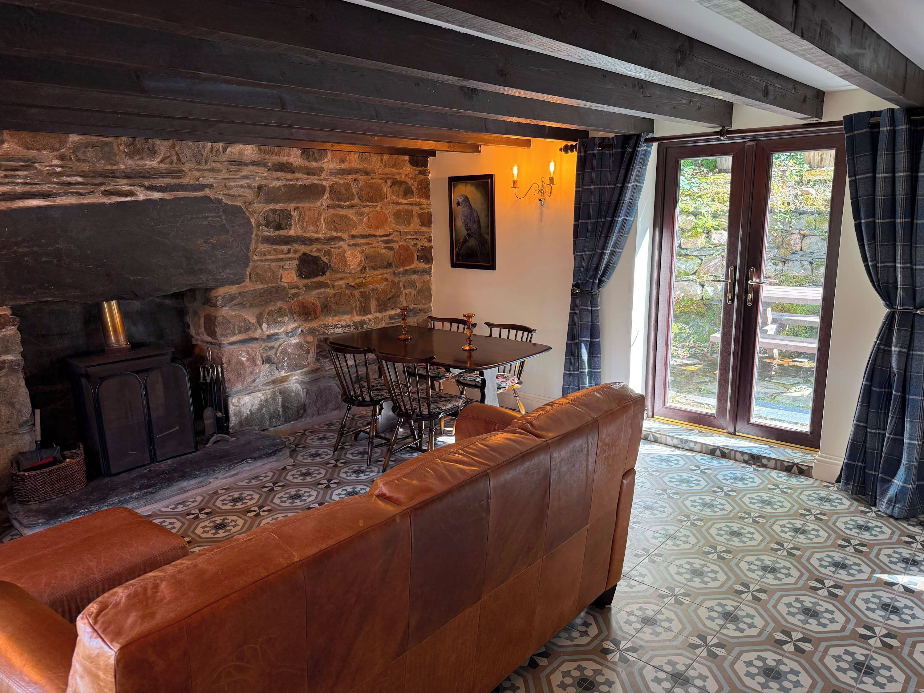 A cozy room with a stone wall, a fireplace, a dining table with chairs, and a leather sofa.