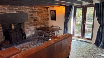 A cozy room with a stone wall, a fireplace, a dining table with chairs, and a leather sofa.