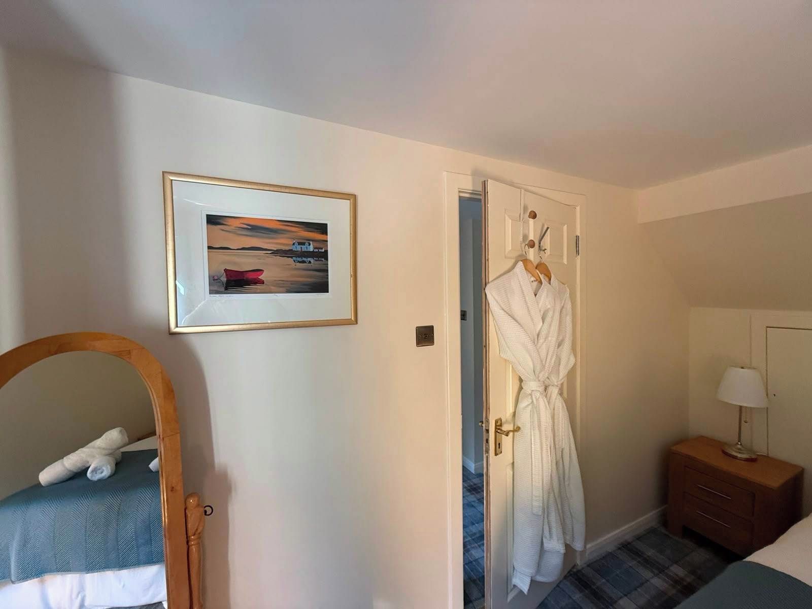 Une chambre d’hôtel avec un lit, une table de chevet avec une lampe, un tableau encadré au mur et un peignoir accroché à la porte.
