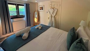 A hotel room with a bed, a window with curtains, a radiator, a mirror, and a robe hanging on the wall. - Stone Cottage, Glencoe, Pet friendly (Glencoe)