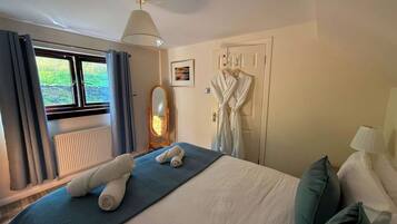 A hotel room with a bed, a window with curtains, a radiator, a mirror, and a robe hanging on the wall.