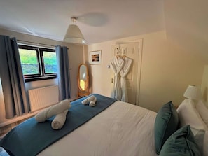 A hotel room with a bed, a window with curtains, a radiator, a mirror, and a robe hanging on the wall. - Stone Cottage, Glencoe, Pet friendly (Glencoe)