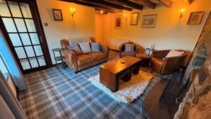 A cozy living room with a sofa, armchairs, a coffee table, and a fireplace. - Stone Cottage, Glencoe, Pet friendly (Glencoe)