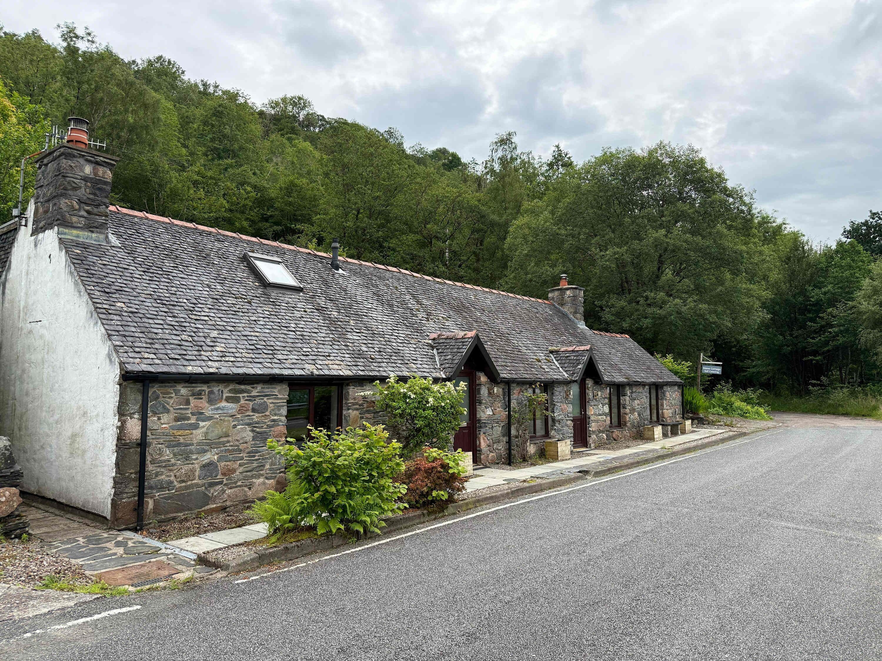 A row of stone cottages with a gravel driveway and a sign indicating a car park.