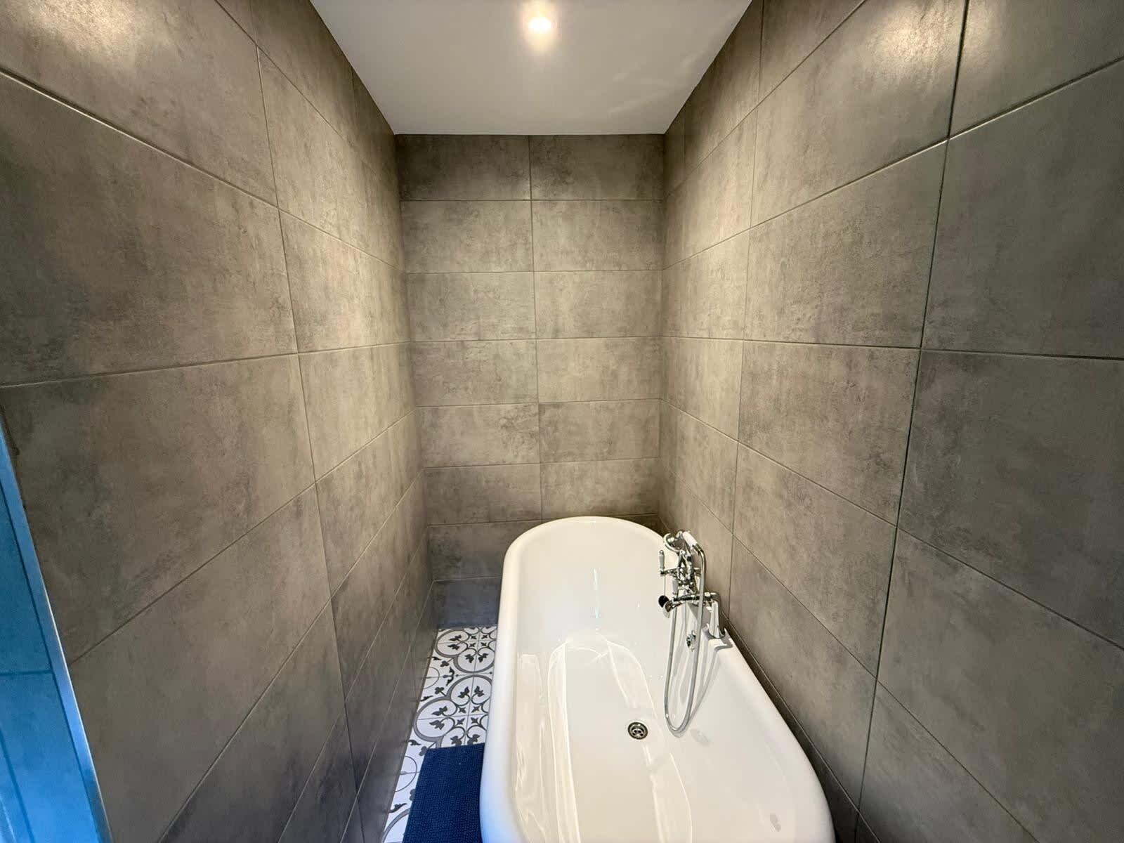 A narrow bathroom with a bathtub, tiled walls, and a patterned floor.