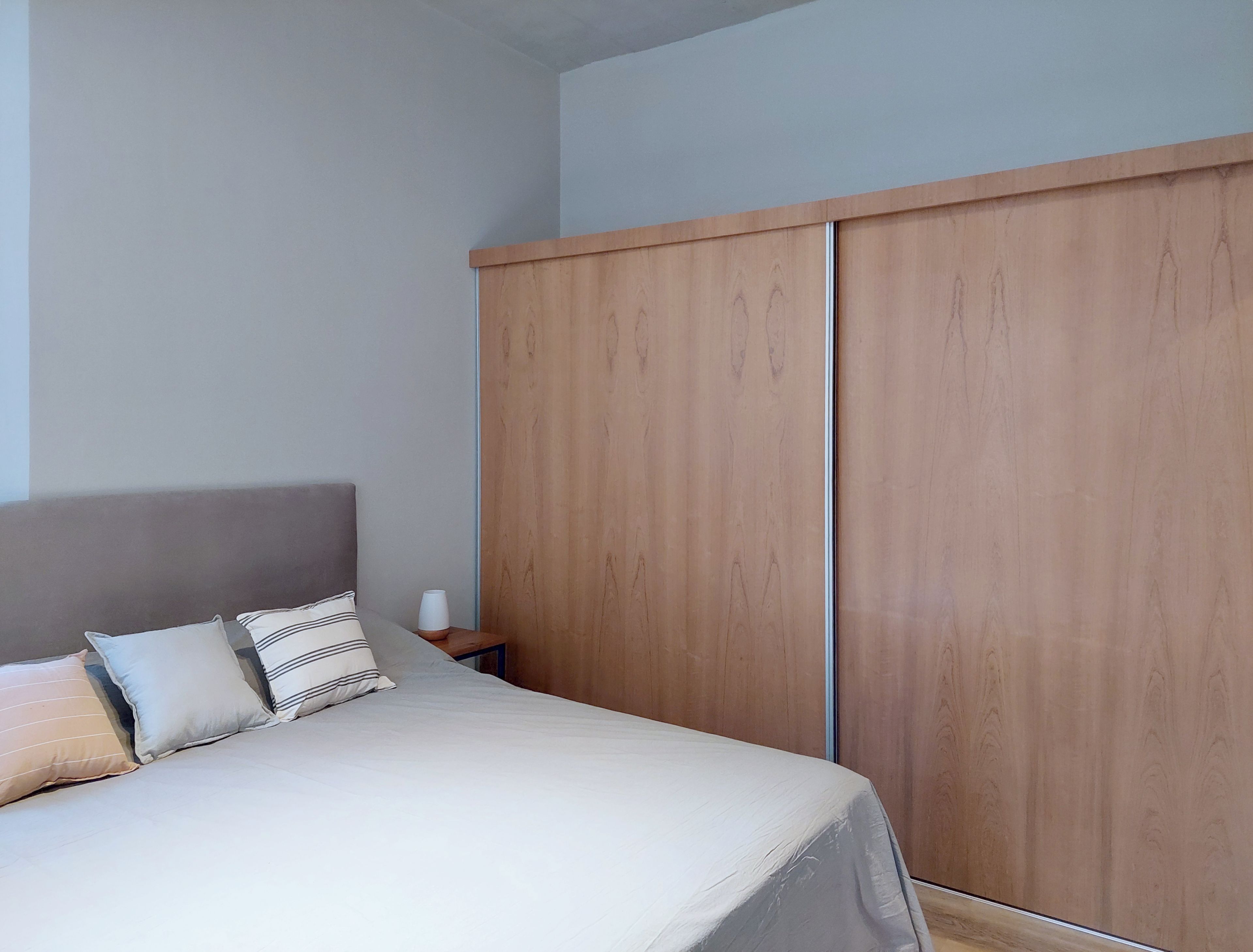 Un dormitorio con cama, almohadas, una mesita de noche y un armario de madera.