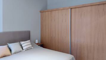 Un dormitorio con cama, almohadas, una mesita de noche y un armario de madera.