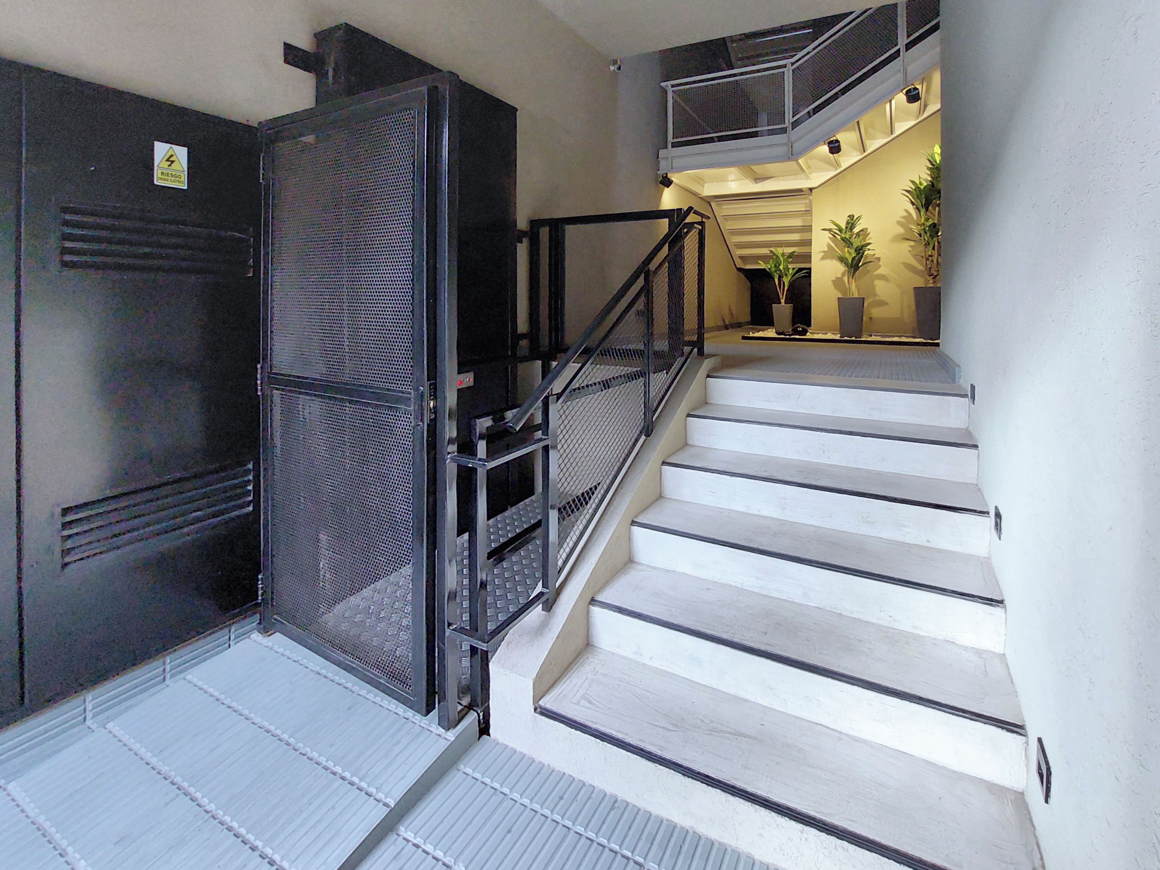 Una escalera con barandales metálicos que lleva a un rellano con una puerta.