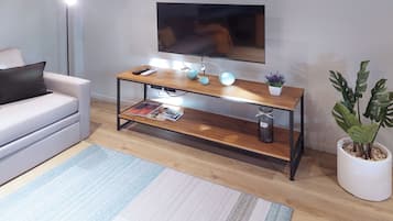 Una sala moderna con un sofá, una mesa de centro de madera con objetos decorativos, un televisor montado en la pared y una planta en maceta.