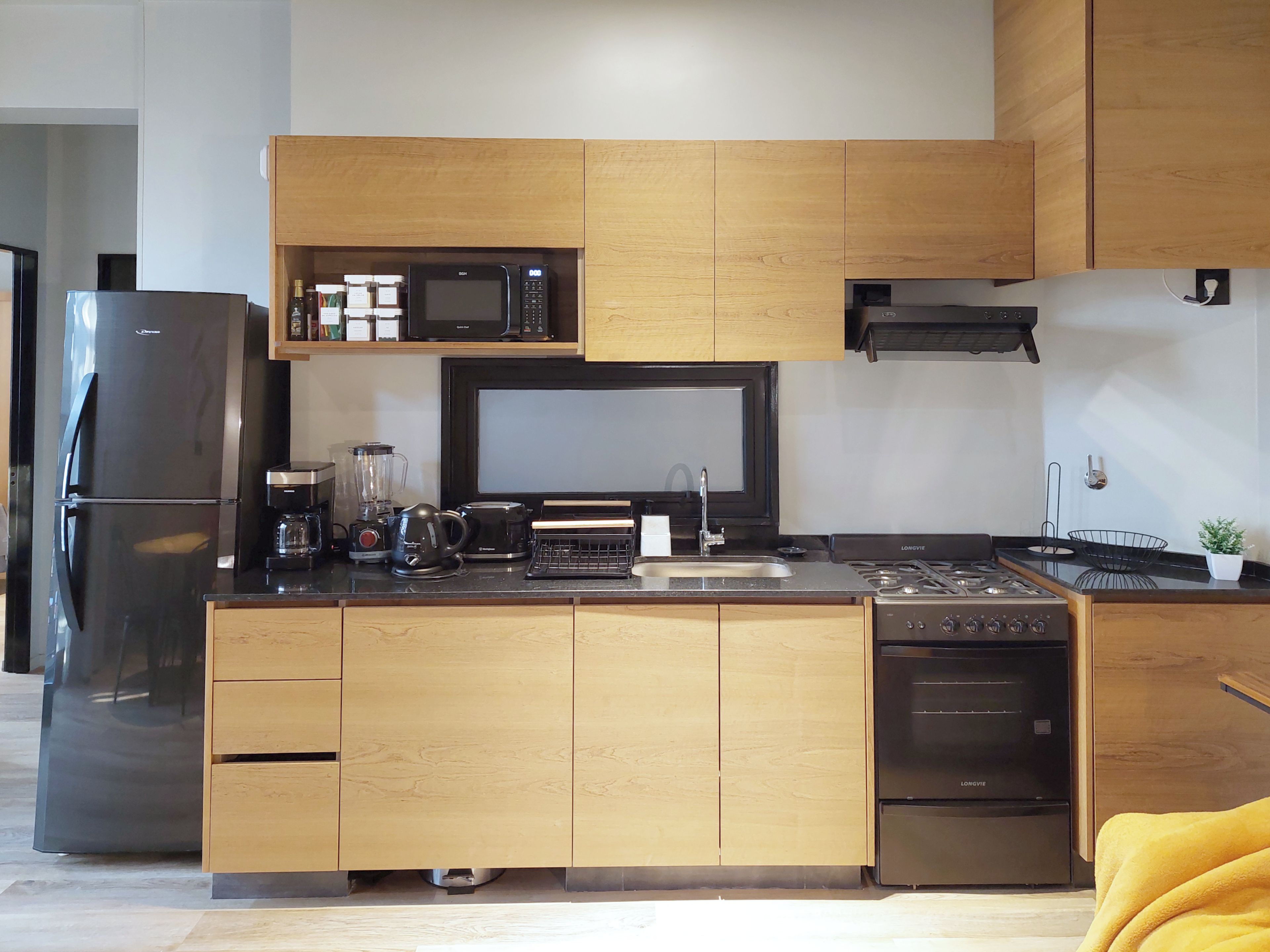 Una cocina moderna con microondas integrado, estufa y lavavajillas, que presenta armarios de madera y un refrigerador negro.