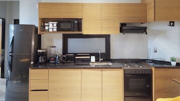 Una cocina moderna con microondas integrado, estufa y lavavajillas, que presenta armarios de madera y un refrigerador negro.