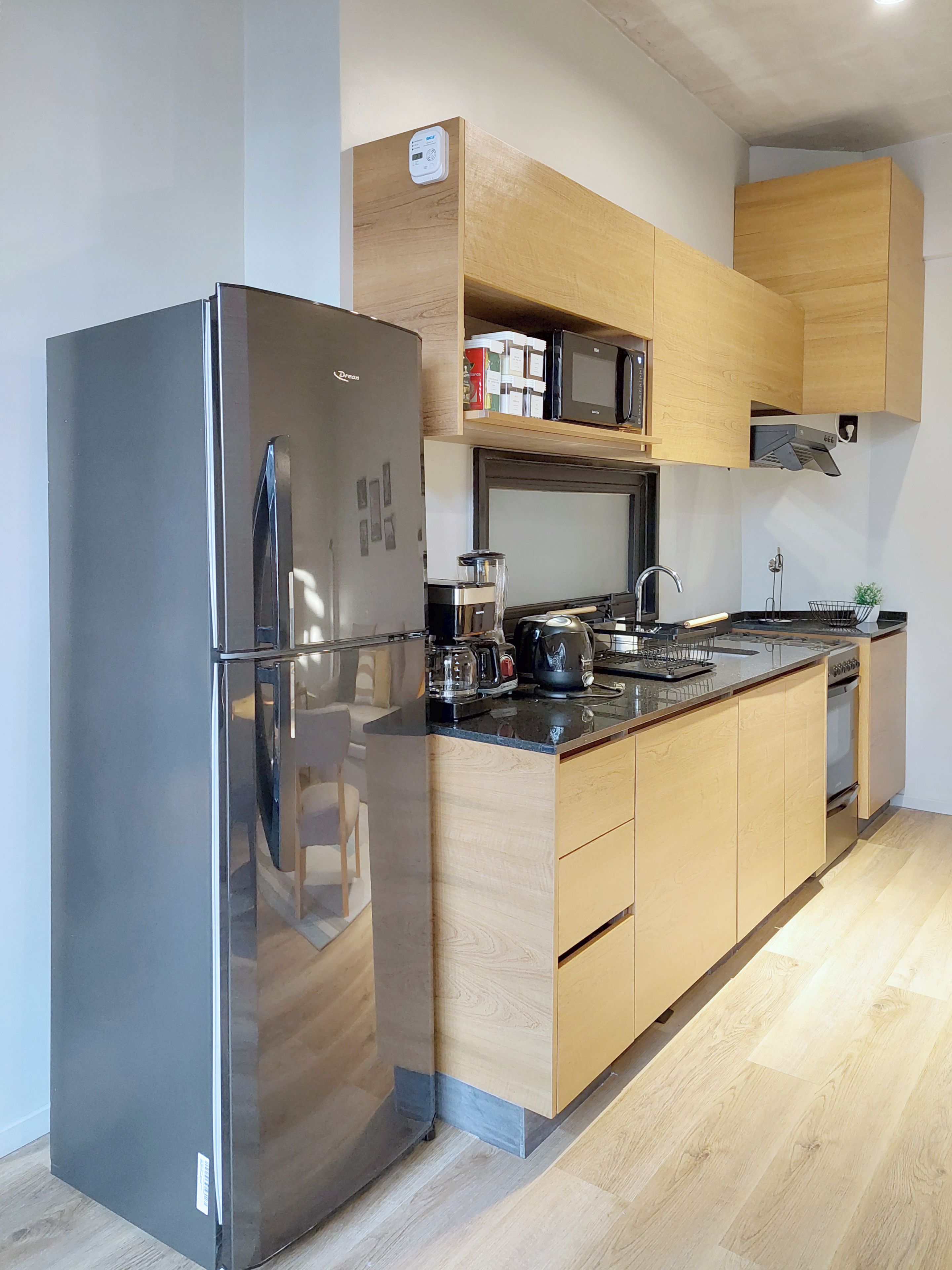 A modern kitchen with a stainless steel refrigerator, wooden cabinets, a microwave, and a stove.