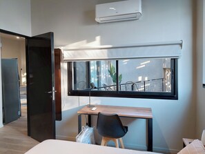 Habitació amb llit, escriptori, cadira, finestra i aire condicionat.