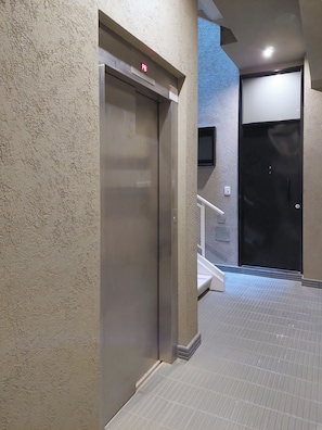 Un ascensor amb una llum indicadora vermella, un televisor fixat a la paret i una porta amb un tancament de seguretat.