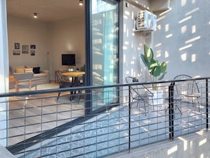 Un interior modern amb zona de menjador, sofà, televisió i balcó amb barana.