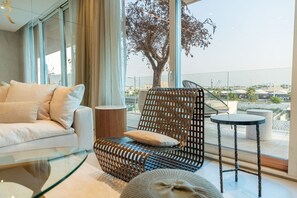 Una sala de estar moderna con un sofá, una silla de mimbre, una mesita y vistas a un árbol y un paisaje urbano a través de amplios ventanales.