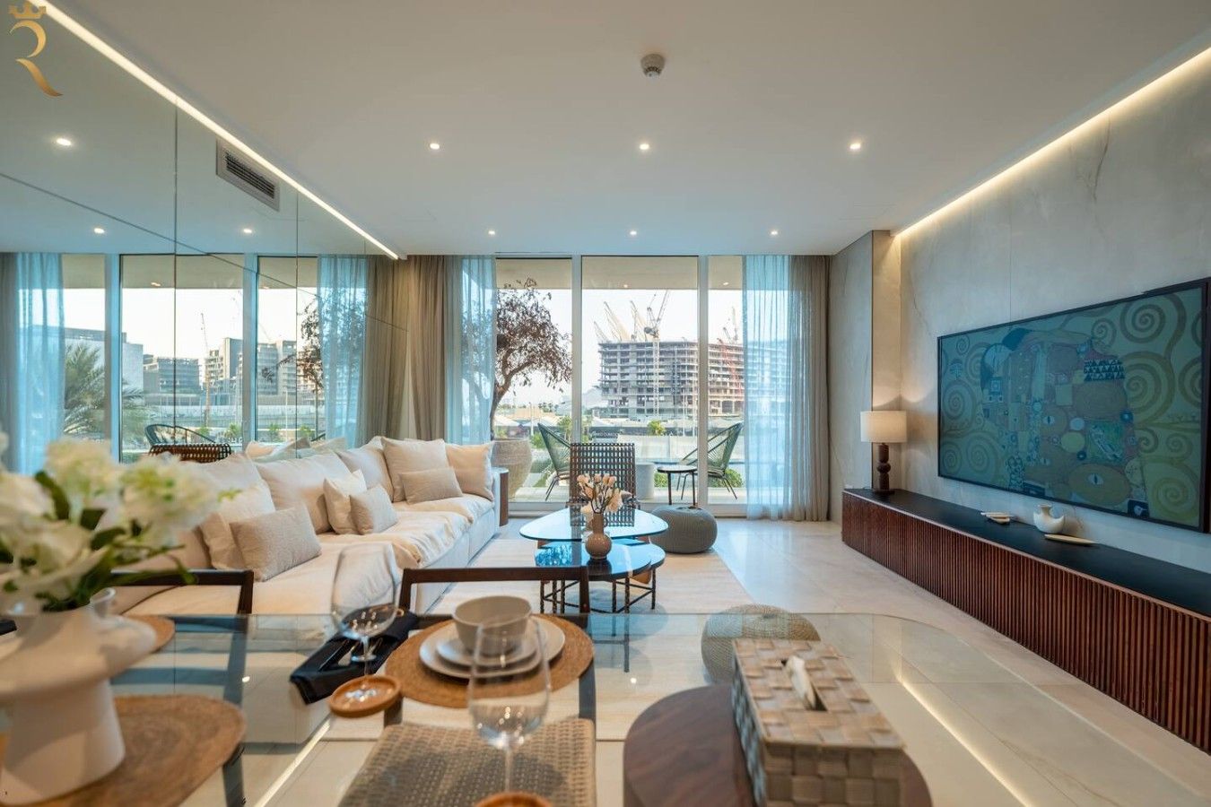 Ein modernes Wohnzimmer mit einer Couch, Esstisch und Stühlen, großen Fenstern mit Blick auf die Stadt und einem an der Wand befestigten Flachbildfernseher.