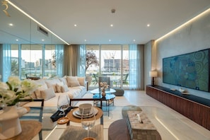 Una sala de estar moderna con sofá, mesa de comedor y sillas, ventanas amplias con vista a la ciudad y un televisor de pantalla plana montado en la pared.