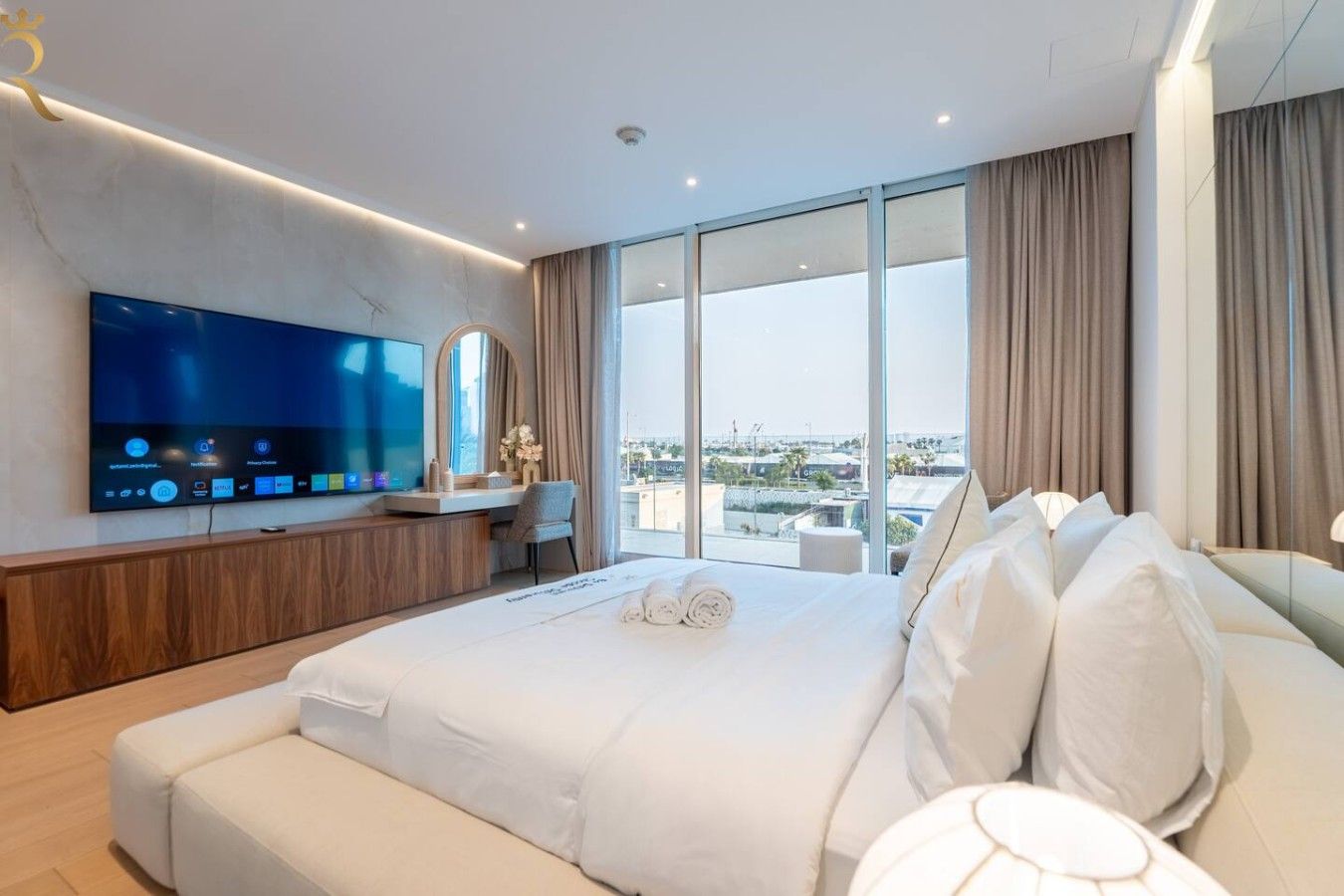 Ein modernes Hotelzimmer mit einem großen Bett, einem Flachbildfernseher, einem Schreibtisch mit Stuhl und Blick auf die Stadt durch große Fenster.