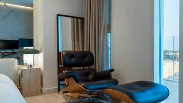 Ein modernes Hotelzimmer mit einem großen Bett, einem Ledersessel, einem Holztischchen, einer Lampe und einem großen Fenster mit Aussicht.