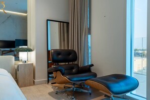 Habitació d'hotel moderna amb un llit gran, una butaca de cuir, una taula auxiliar de fusta, una làmpada i una finestra ampla amb vistes.
