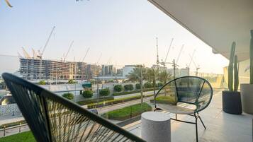A balcony with two chairs, a cactus, and a view of a construction site with cranes.