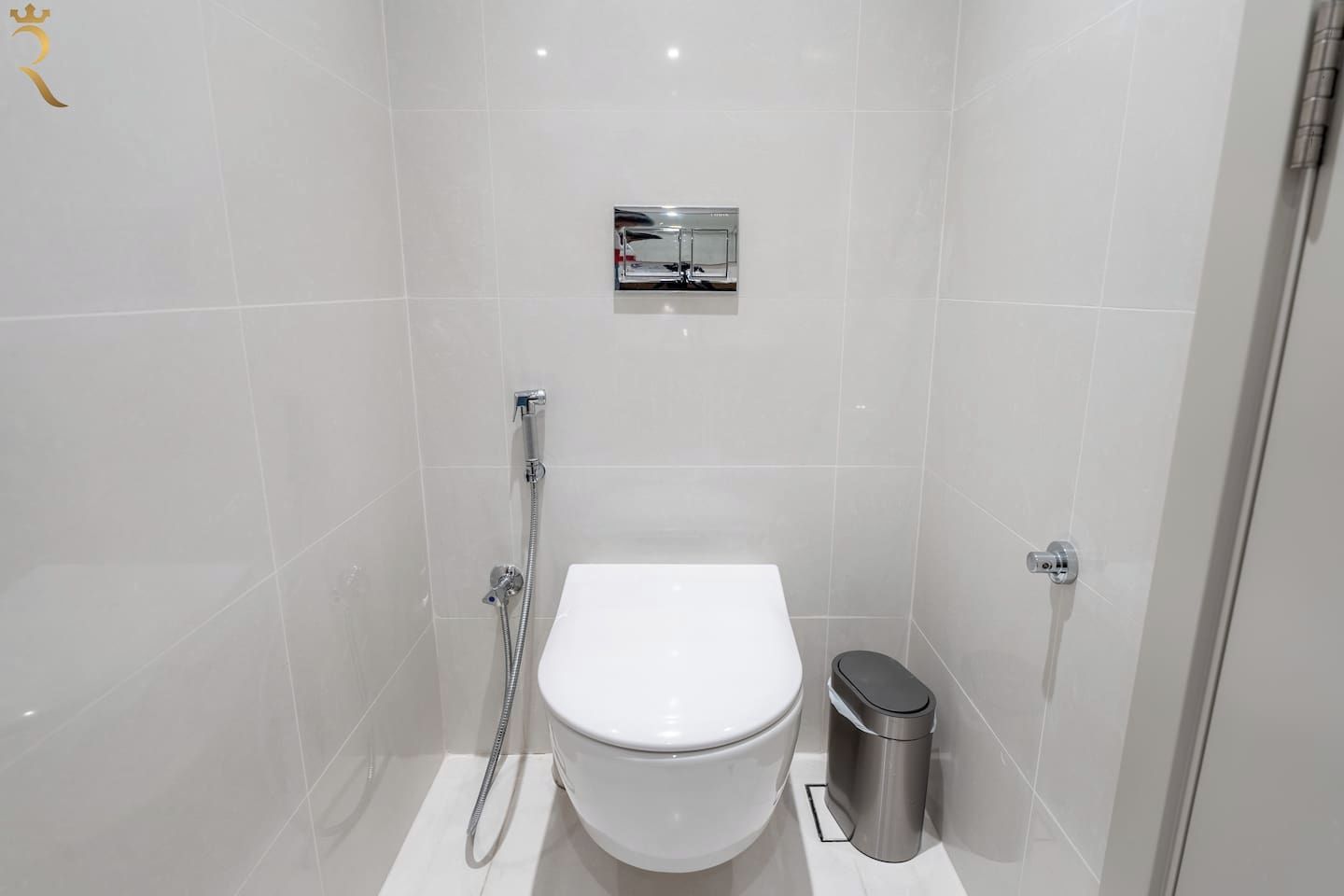 Ein modernes Badezimmer mit Toilette in Weiß, einem Edelstahl-Mülleimer und einer Duschkabine.