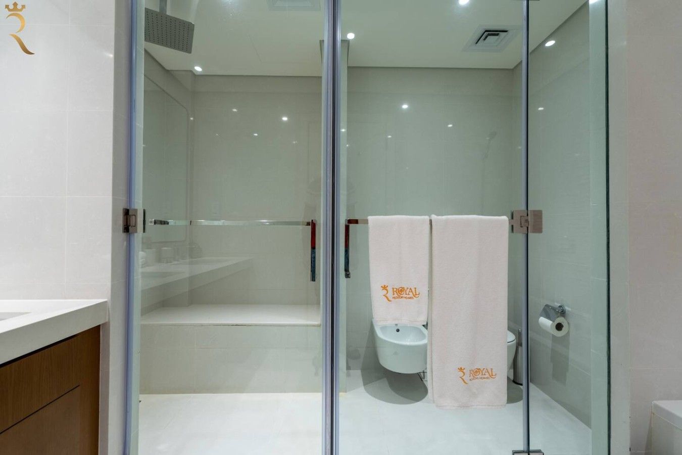 Une salle de bain moderne avec une paroi en verre, un espace douche et deux toilettes équipées de serviettes.