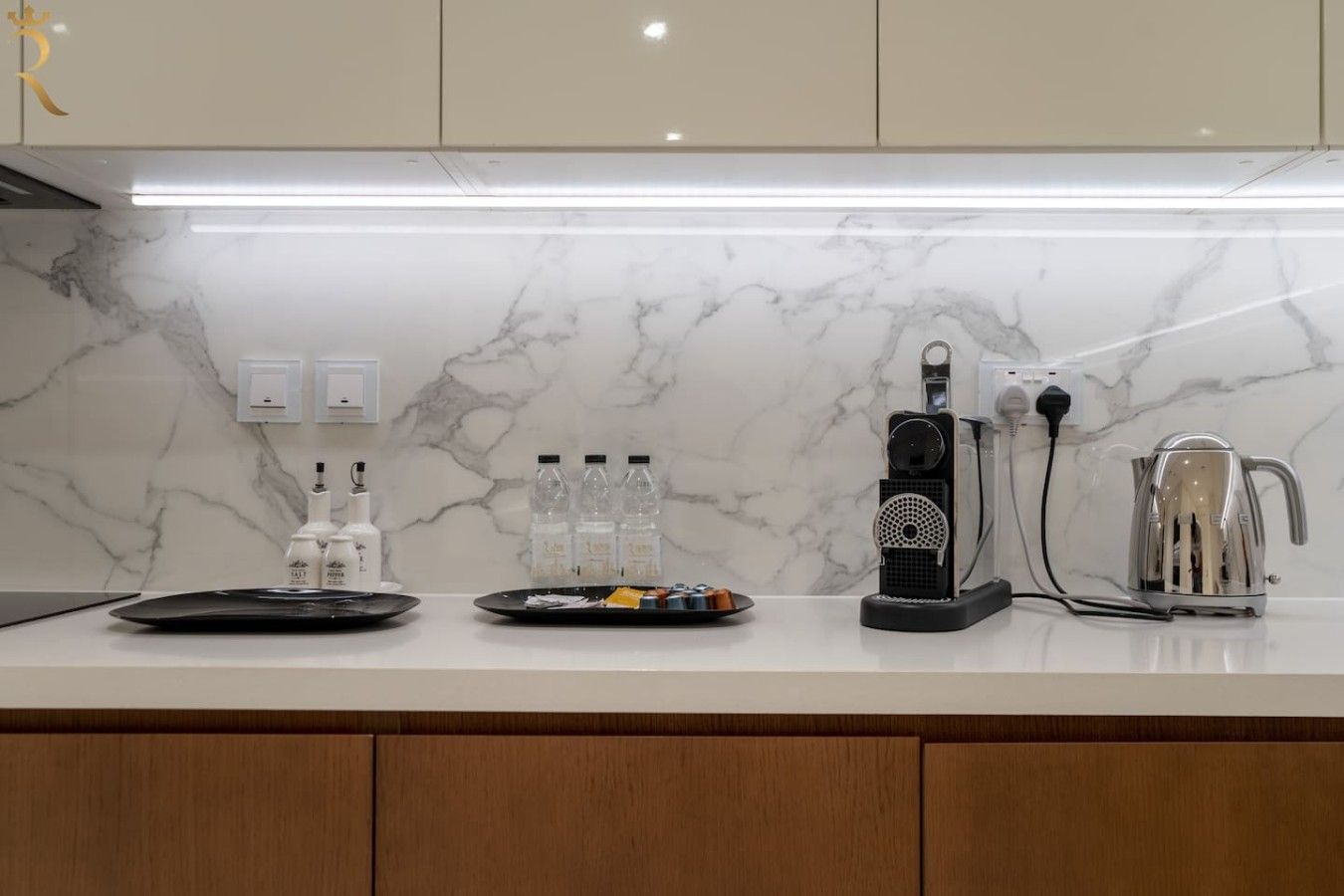 Eine moderne Küche mit Marmorarbeitsplatten, einer Kaffeemaschine, einem Wasserkocher und einem Wasserspender.