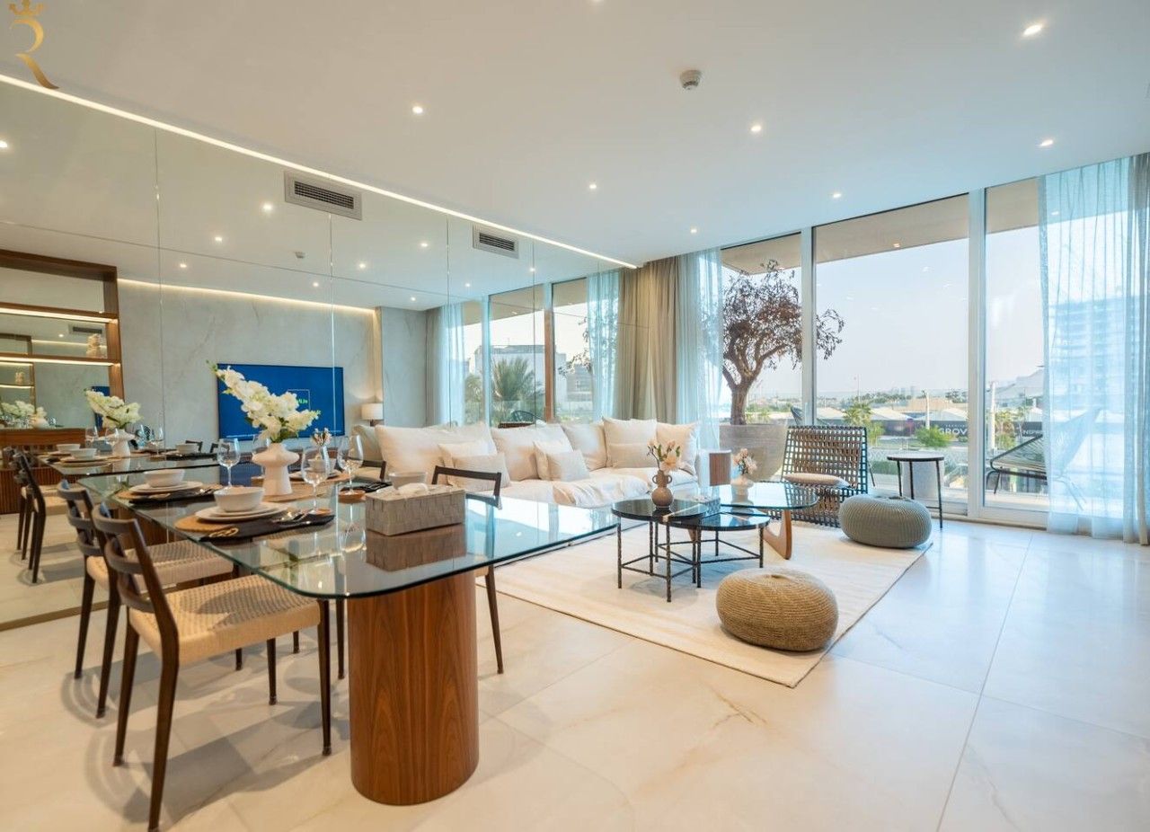 A spacious living area with a glass dining table, comfortable seating, and large windows offering a view of the city.