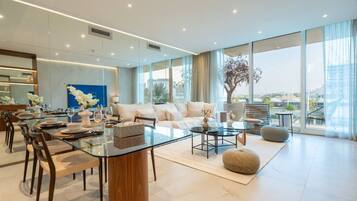 A spacious living area with a glass dining table, comfortable seating, and large windows offering a view of the city.