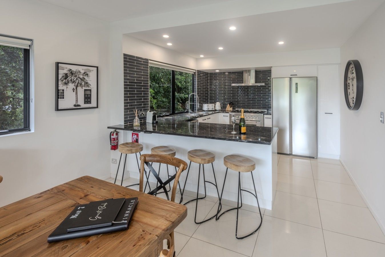 A modern kitchen with a central island, bar stools, a dining table, and a framed picture on the wall.