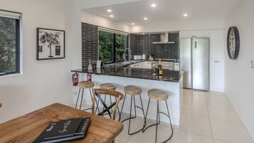 A modern kitchen with a central island, bar stools, a dining table, and a framed picture on the wall.