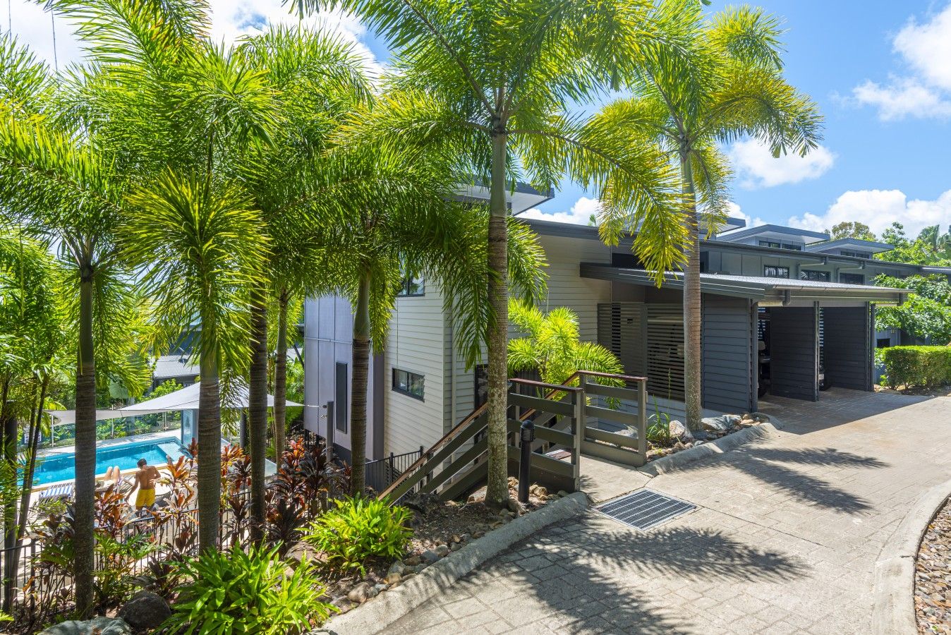 A modern building with a pool, surrounded by palm trees and a well-maintained garden.