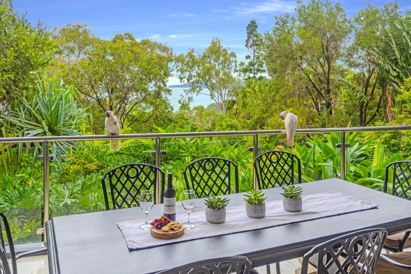 An outdoor dining area with a table set for two, surrounded by lush greenery and trees.
